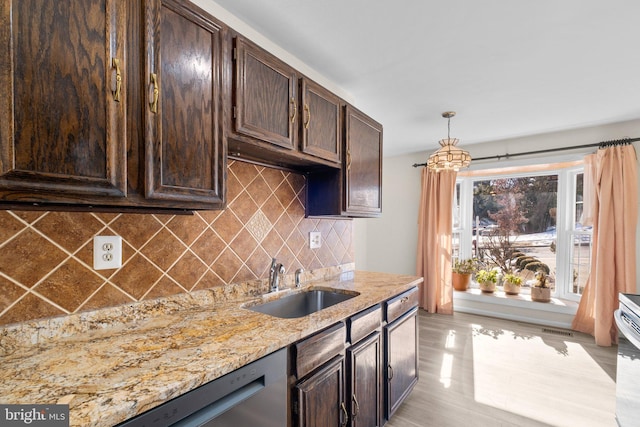 kitchen with dark brown cabinetry, sink, decorative light fixtures, and light stone counters