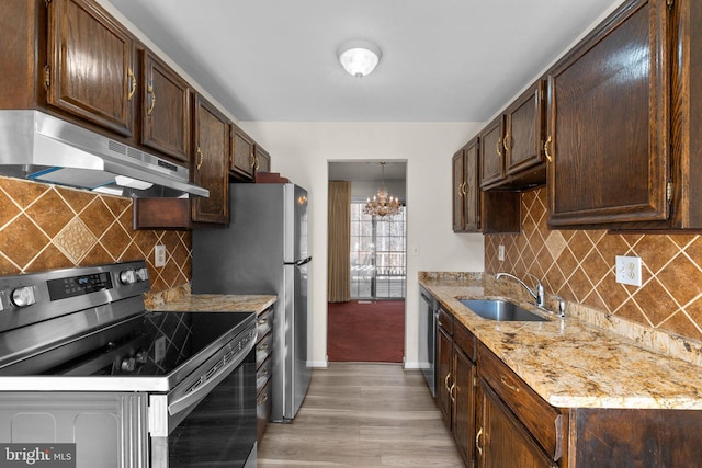 kitchen with dark brown cabinetry, sink, light wood-type flooring, appliances with stainless steel finishes, and light stone countertops