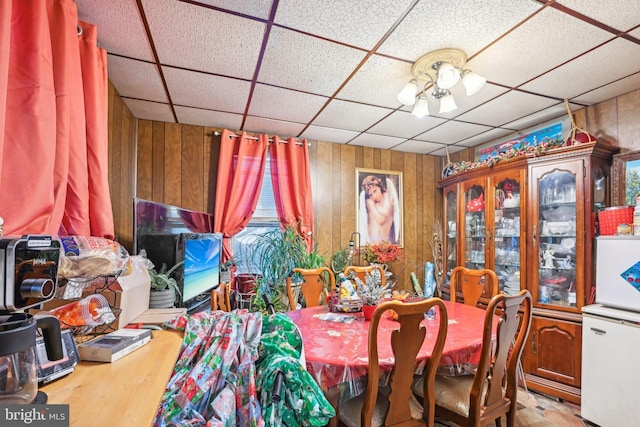 dining room with hardwood / wood-style floors, a drop ceiling, and wood walls