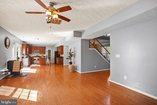 unfurnished living room featuring a wealth of natural light, ceiling fan, light hardwood / wood-style floors, and a textured ceiling