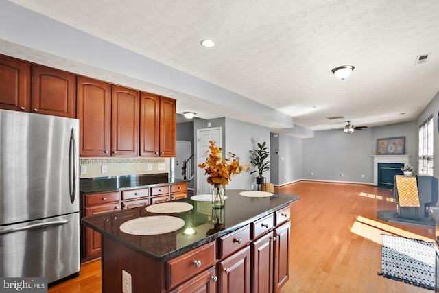 kitchen featuring ceiling fan, a kitchen island, a textured ceiling, light hardwood / wood-style floors, and stainless steel refrigerator