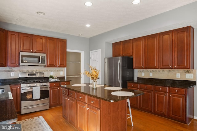 kitchen with dark stone counters, light hardwood / wood-style flooring, decorative backsplash, a kitchen island, and stainless steel appliances