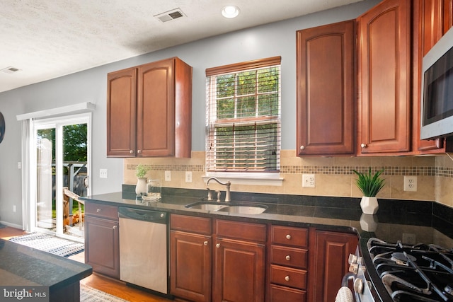 kitchen with appliances with stainless steel finishes, tasteful backsplash, a textured ceiling, sink, and light hardwood / wood-style floors