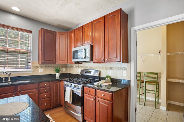 kitchen with appliances with stainless steel finishes, light tile patterned floors, dark stone counters, and sink