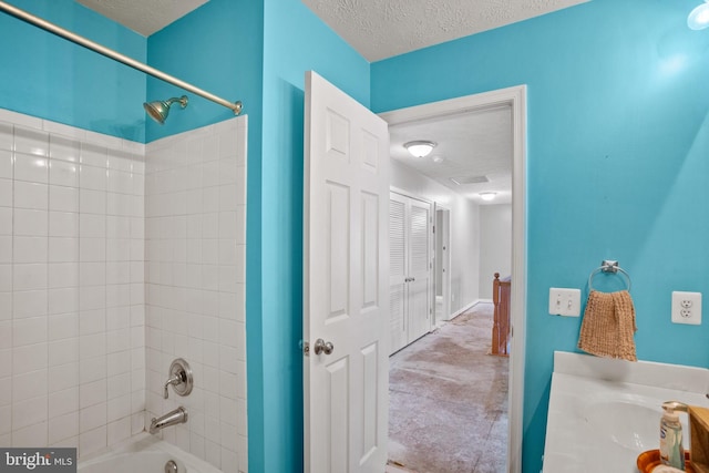 bathroom featuring a textured ceiling, vanity, and tiled shower / bath