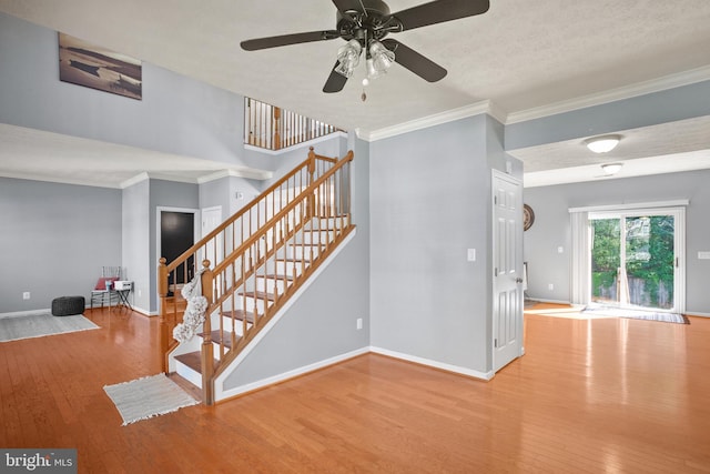 stairs featuring ceiling fan, crown molding, wood-type flooring, and a textured ceiling