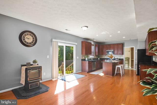 kitchen featuring a kitchen breakfast bar, a textured ceiling, stainless steel appliances, light hardwood / wood-style flooring, and a kitchen island