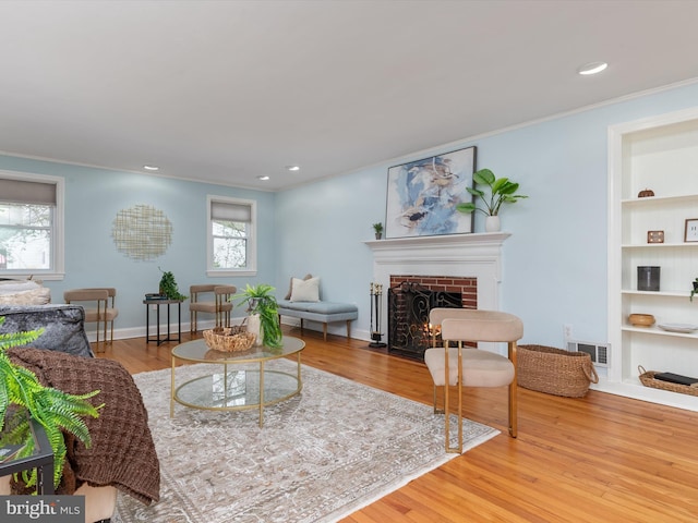 living room with wood-type flooring, a brick fireplace, ornamental molding, and a healthy amount of sunlight