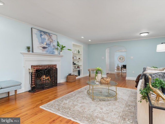 living room featuring hardwood / wood-style floors, crown molding, built in features, and a fireplace