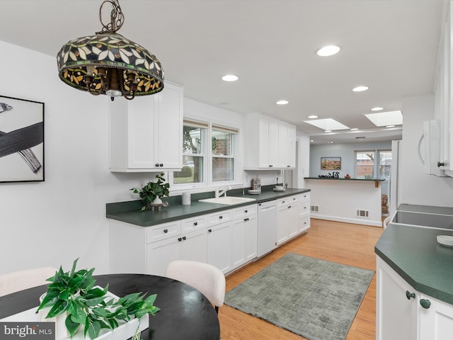 kitchen with dishwasher, a skylight, white cabinets, and light hardwood / wood-style floors