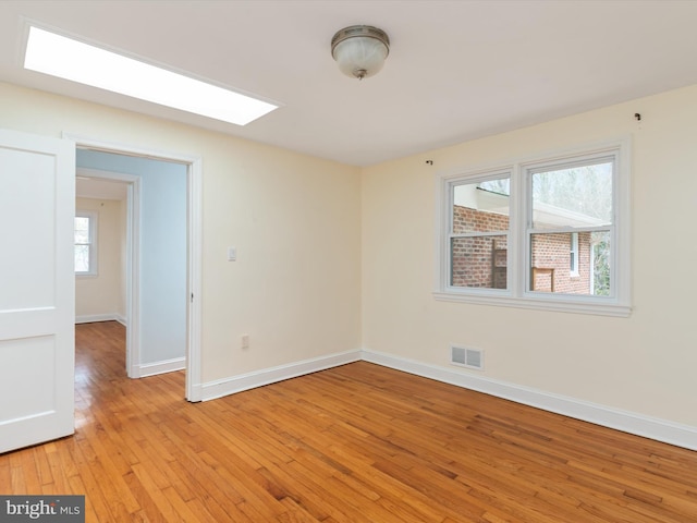 empty room with a skylight and light hardwood / wood-style flooring