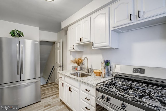 kitchen featuring stainless steel appliances, sink, white cabinetry, light hardwood / wood-style flooring, and light stone countertops