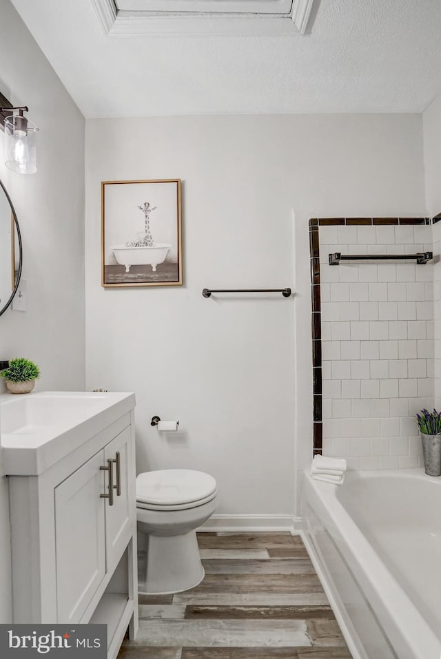 full bathroom featuring toilet, wood-type flooring, vanity, tiled shower / bath, and a textured ceiling