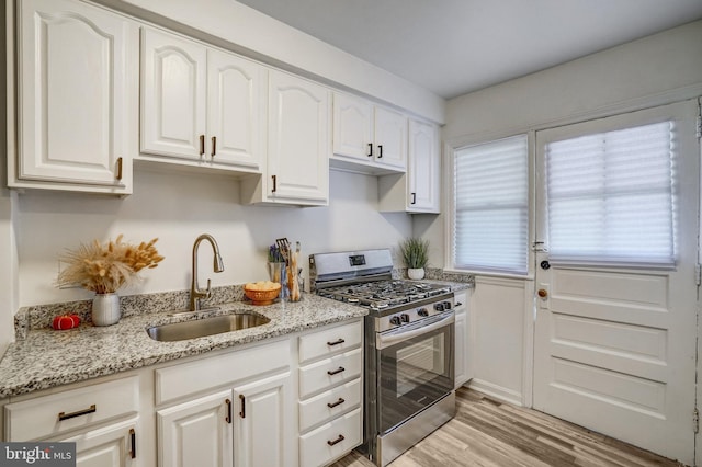 kitchen with sink, white cabinets, light stone countertops, and stainless steel gas range oven