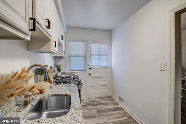 kitchen with sink, light hardwood / wood-style floors, white cabinetry, and light stone countertops