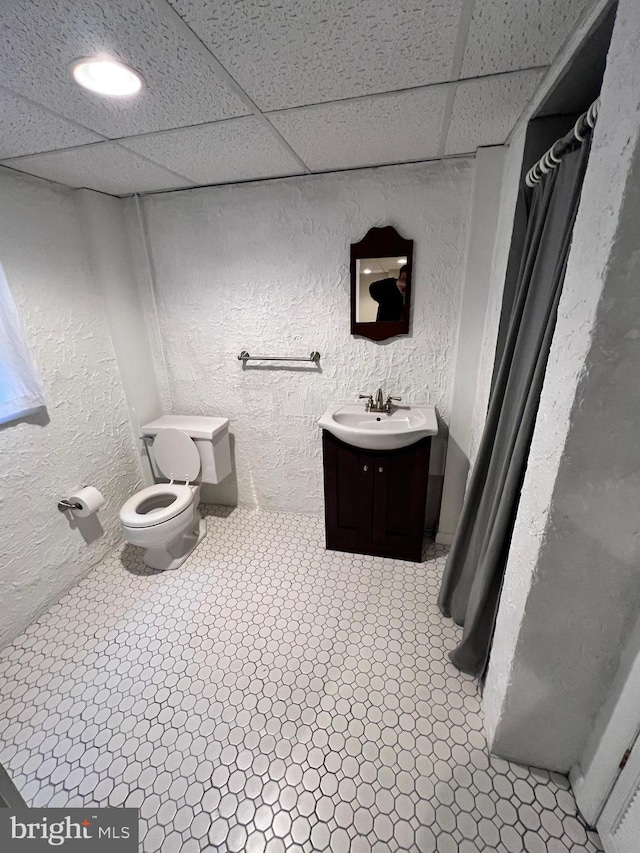 bathroom featuring tile patterned floors, vanity, toilet, and a drop ceiling