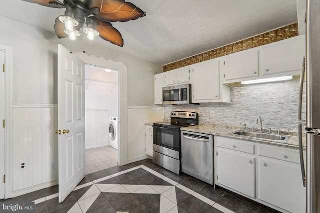 kitchen with washer / dryer, dark tile patterned floors, white cabinetry, sink, and stainless steel appliances