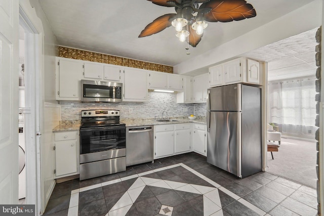 kitchen with sink, white cabinets, light stone countertops, dark colored carpet, and stainless steel appliances