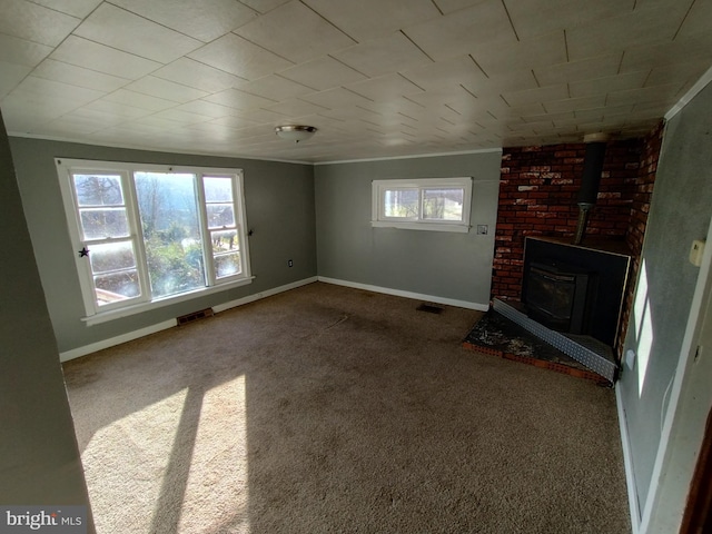 unfurnished living room featuring carpet flooring, a wood stove, and ornamental molding