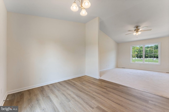 empty room with ceiling fan with notable chandelier, light hardwood / wood-style floors, and lofted ceiling