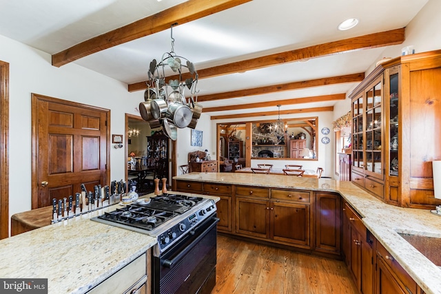 kitchen featuring range with gas cooktop, light stone counters, decorative light fixtures, a notable chandelier, and beamed ceiling