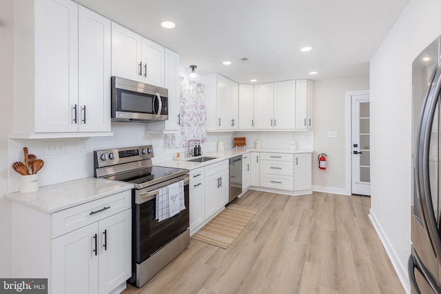 kitchen featuring light hardwood / wood-style floors, decorative backsplash, sink, stainless steel appliances, and white cabinets