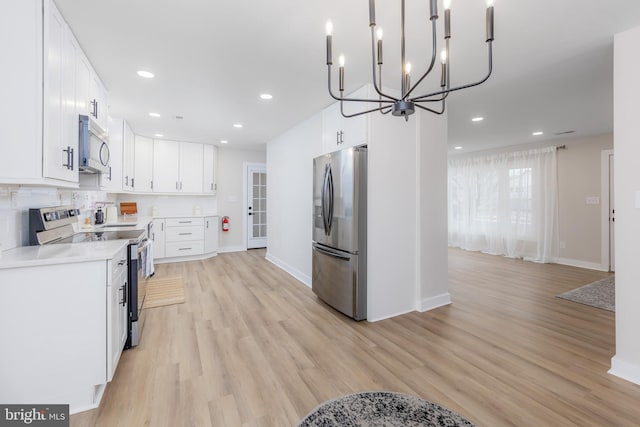 kitchen with an inviting chandelier, stainless steel appliances, decorative light fixtures, light wood-type flooring, and white cabinets