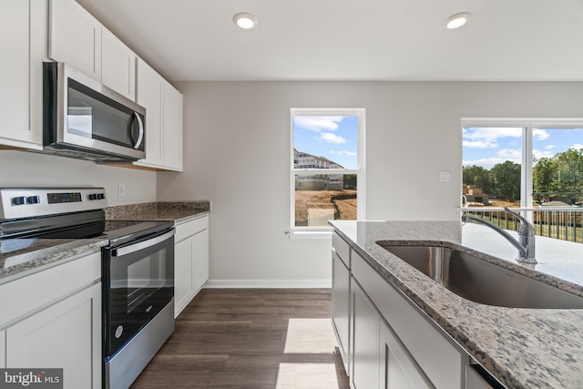 kitchen with dark wood-type flooring, white cabinets, sink, light stone countertops, and stainless steel appliances