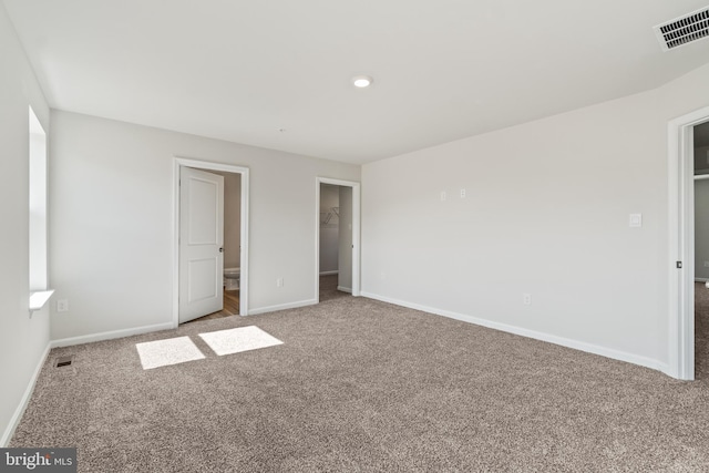 unfurnished bedroom with a walk in closet, ensuite bathroom, a closet, and carpet floors