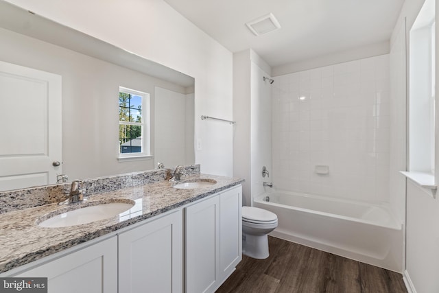 full bathroom with hardwood / wood-style floors, vanity, tiled shower / bath combo, and toilet