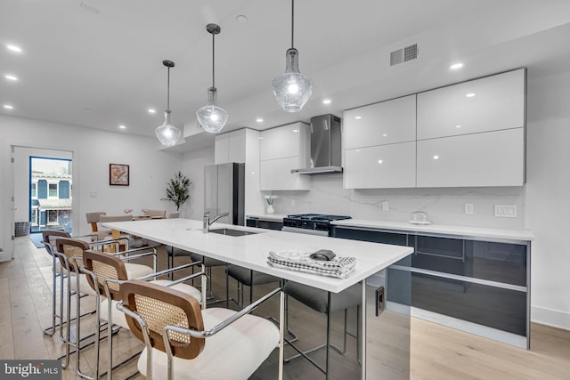 kitchen with decorative light fixtures, stainless steel fridge, wall chimney range hood, a kitchen island with sink, and stove