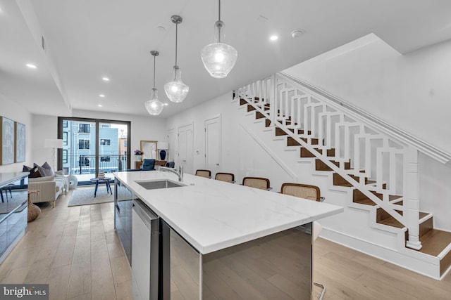 kitchen featuring an island with sink, sink, pendant lighting, and light hardwood / wood-style flooring