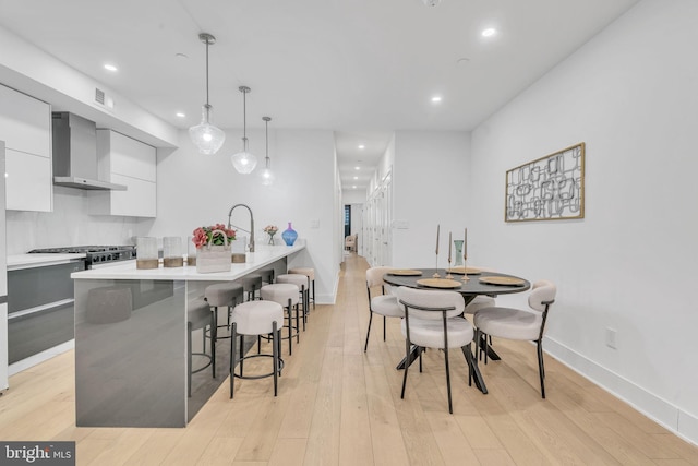 kitchen with white cabinetry, hanging light fixtures, light wood-type flooring, a kitchen breakfast bar, and wall chimney range hood