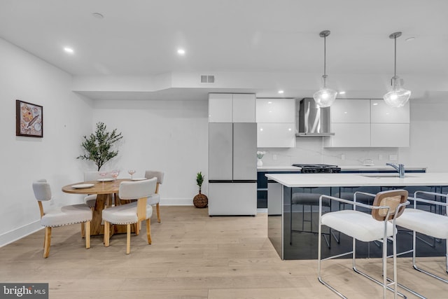 kitchen with sink, white cabinetry, fridge, pendant lighting, and wall chimney range hood