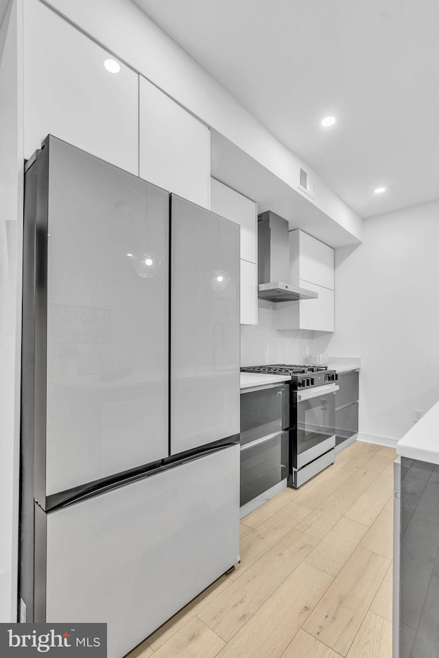 kitchen featuring refrigerator, gray cabinetry, light hardwood / wood-style floors, gas range, and wall chimney range hood