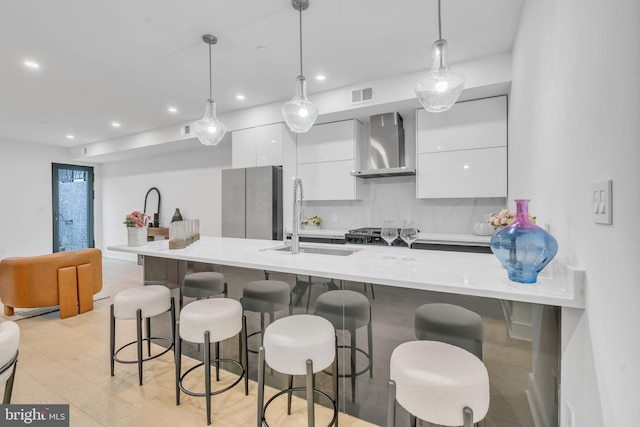 kitchen featuring wall chimney range hood, stainless steel fridge, hanging light fixtures, and a breakfast bar