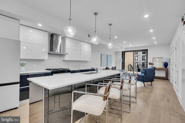 kitchen featuring sink, wall chimney range hood, an island with sink, decorative light fixtures, and white fridge