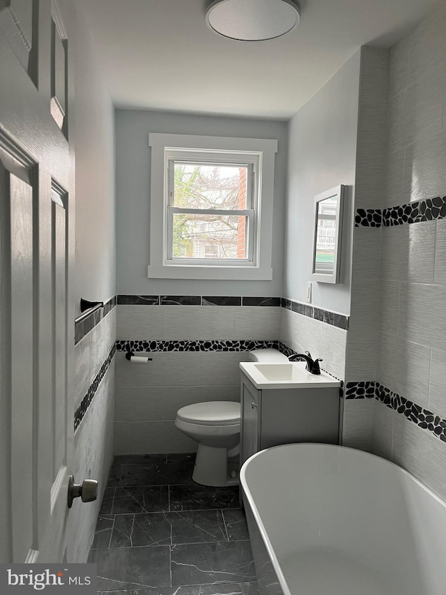 bathroom featuring vanity, a bath, tile walls, and toilet