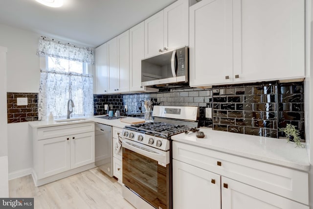 kitchen with white cabinets, stainless steel appliances, decorative backsplash, sink, and light hardwood / wood-style flooring