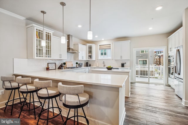 kitchen featuring white cabinetry, a breakfast bar, wall chimney range hood, and kitchen peninsula