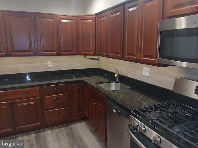 kitchen with appliances with stainless steel finishes, light hardwood / wood-style flooring, dark stone countertops, and sink