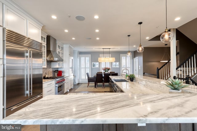 kitchen with high quality appliances, a large island, white cabinets, and wall chimney exhaust hood