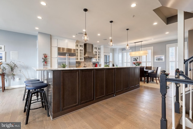 kitchen with a large island, stainless steel built in refrigerator, decorative light fixtures, and wall chimney range hood