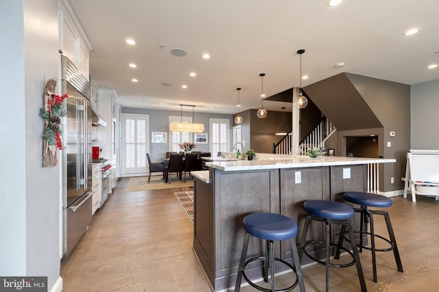 kitchen with a breakfast bar area, a spacious island, white cabinets, decorative light fixtures, and light wood-type flooring