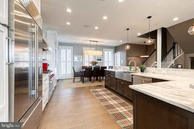 kitchen featuring sink, high end appliances, light stone counters, light hardwood / wood-style flooring, and pendant lighting