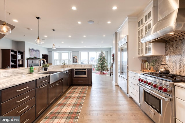 kitchen with pendant lighting, high quality appliances, sink, white cabinets, and exhaust hood