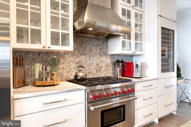 kitchen featuring wall chimney range hood, appliances with stainless steel finishes, backsplash, white cabinets, and beverage cooler