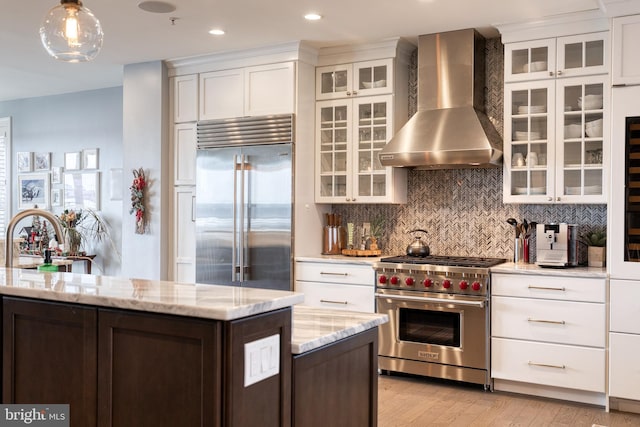 kitchen with high end appliances, light stone counters, decorative light fixtures, and wall chimney exhaust hood