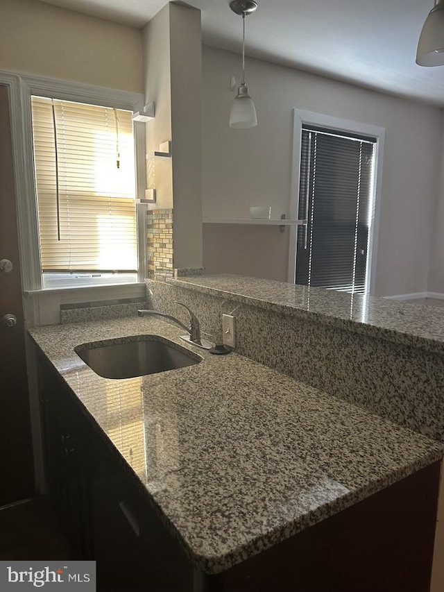 kitchen featuring decorative light fixtures, light stone countertops, and sink