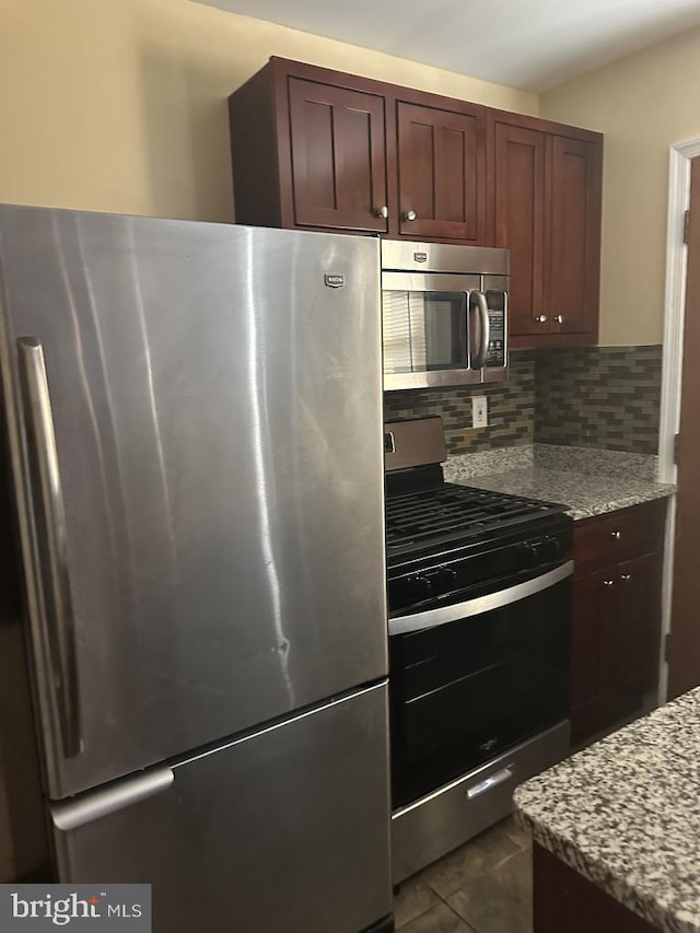 kitchen with tasteful backsplash, light stone counters, stainless steel appliances, and dark tile patterned flooring